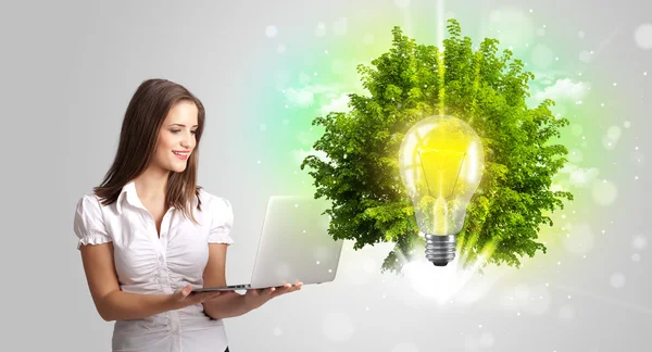 Ung flicka som presenterar idé glödlampa med grönt träd — Stockfoto