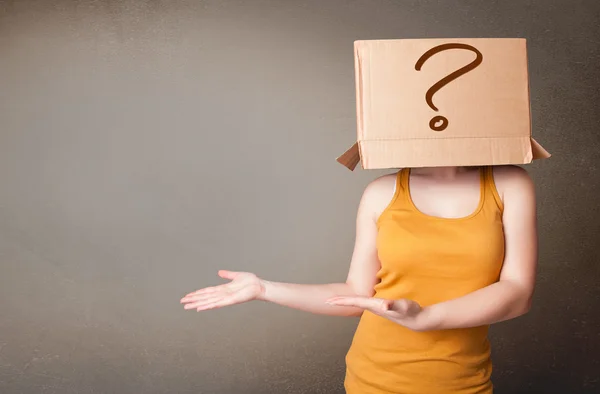 Young lady gesturing with a cardboard box on her head with quest — Stock Photo, Image