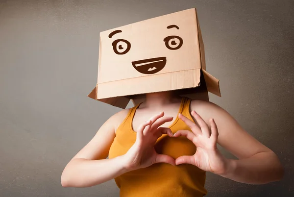 Mujer joven haciendo gestos con una caja de cartón en la cabeza con una sonrisa — Foto de Stock