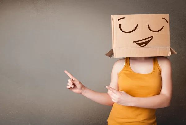 Jonge vrouw met een kartonnen doos op haar hoofd met smil gebaren — Stockfoto