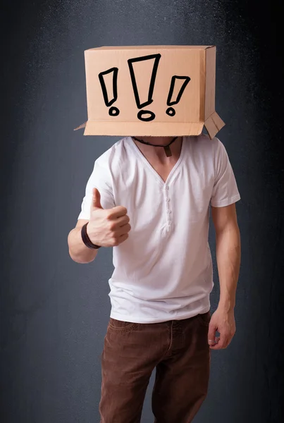 Young man gesturing with a cardboard box on his head with exclam — Stock Photo, Image