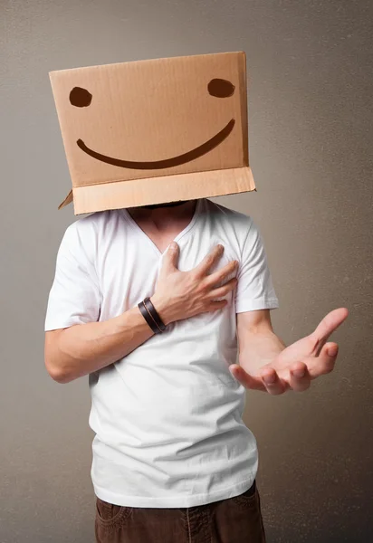 Young man gesturing with a cardboard box on his head with smiley — Stock Photo, Image