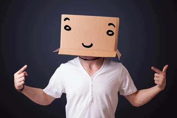 Young man gesturing with a cardboard box on his head with smiley — Stock Photo, Image