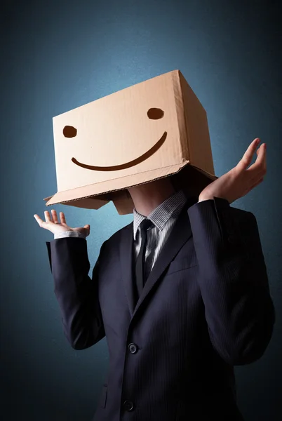 Uomo d'affari gesticolando con una scatola di cartone in testa con smil — Foto Stock