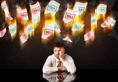 Depresyondaki işadamı yanan vergi ve fatura kağıtlarının altında oturuyor