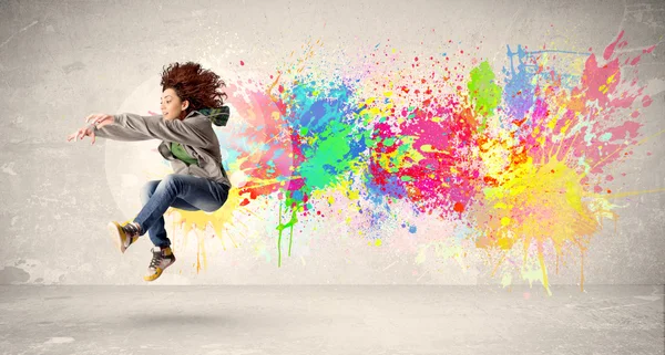 Feliz adolescente saltando con salpicaduras de tinta de colores en el respaldo urbano — Foto de Stock