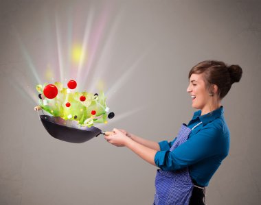 Genç bir kadın taze sebze pişiriyor.