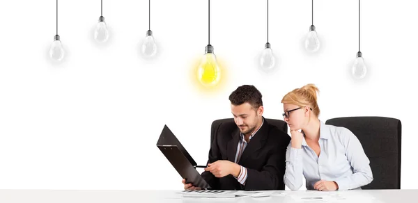 Business man and woman sitting at table with idea light bulbs — Stock Photo, Image