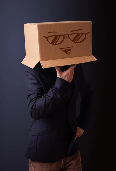 Young man gesturing with a cardboard box on his head with smiley — Stock Photo, Image