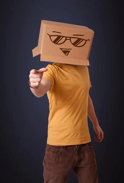 Joven haciendo un gesto con una caja de cartón en la cabeza con sonriente — Foto de Stock