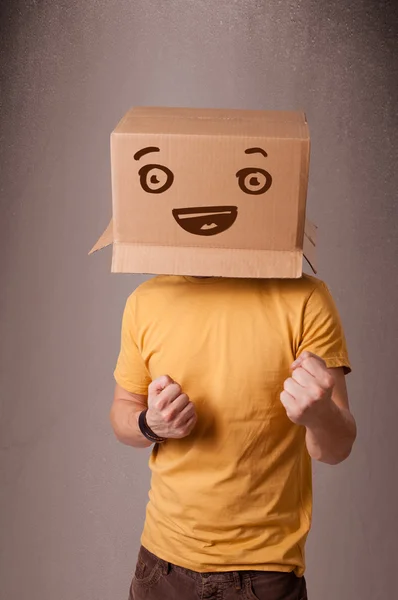 Joven haciendo un gesto con una caja de cartón en la cabeza con sonriente — Foto de Stock