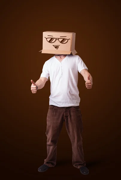 Young man gesturing with a cardboard box on his head with smiley — Stock Photo, Image