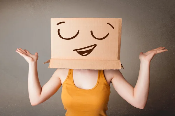 Young woman gesturing with a cardboard box on her head with smil — Stock Photo, Image