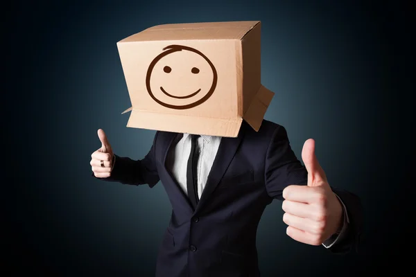 Affärsman gestikulerande med en kartong på hans huvud med smil — Stockfoto