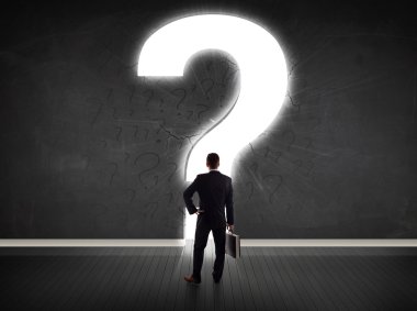 Parlak bir soru işaretiyle duvara bakan bir iş adamı 