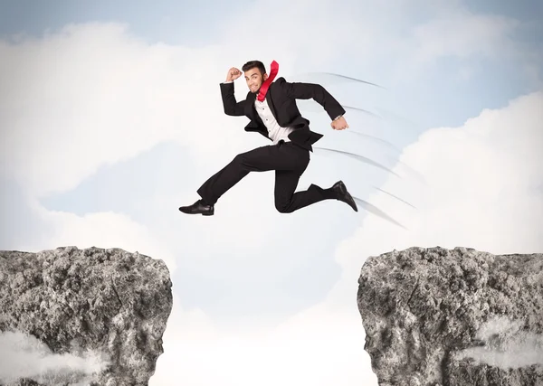 Grappige zakenman springen over rotsen met kloof — Stockfoto