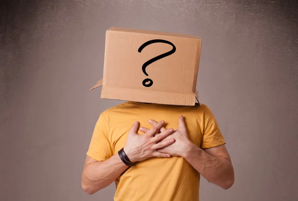 Young man gesturing with a cardboard box on his head with questi — Stock Photo, Image