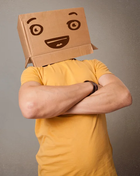 Young man gesturing with a cardboard box on his head with smiley — Stock Photo, Image