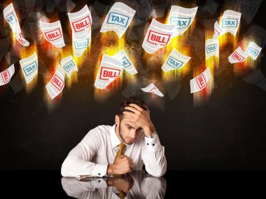 Depresyondaki işadamı yanan vergi ve fatura kağıtlarının altında oturuyor