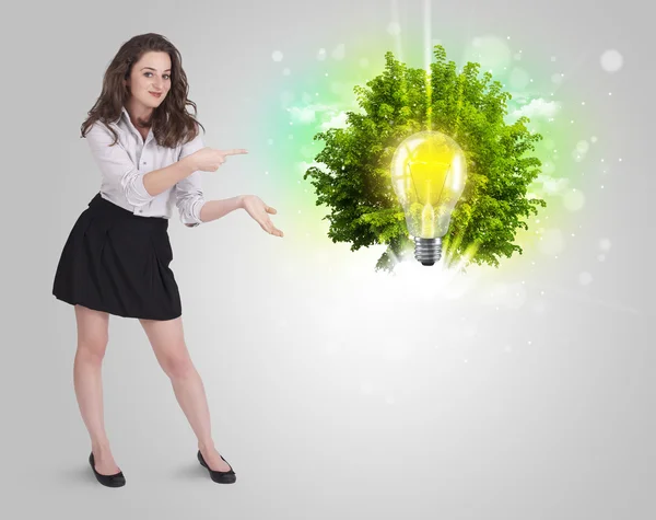 Chica joven presentando idea bombilla con árbol verde —  Fotos de Stock