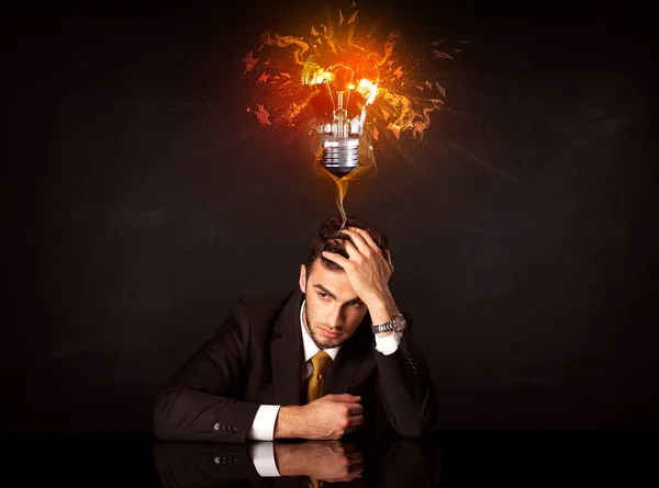 Businessman sitting under a blowing idea bulb — Stock Photo, Image