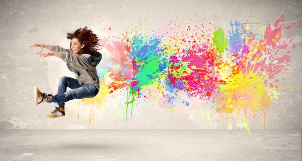 Feliz adolescente saltando con salpicaduras de tinta de colores en el respaldo urbano — Foto de Stock