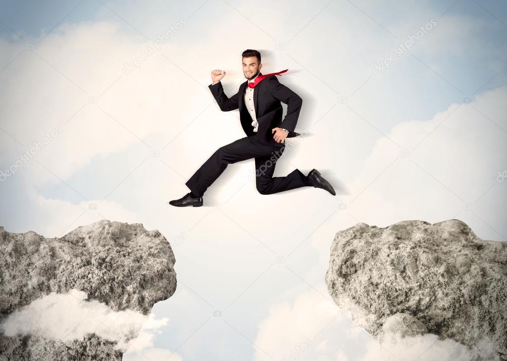 Happy business man jumping over a cliff 