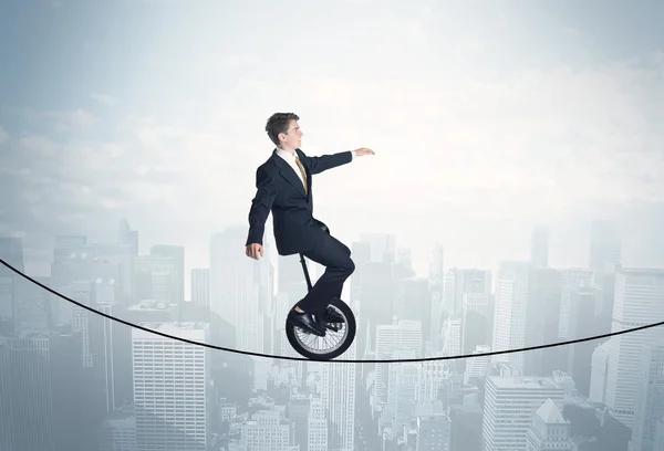 Brave guy riding a monocycle on a rope above cityscape — Stock Photo, Image