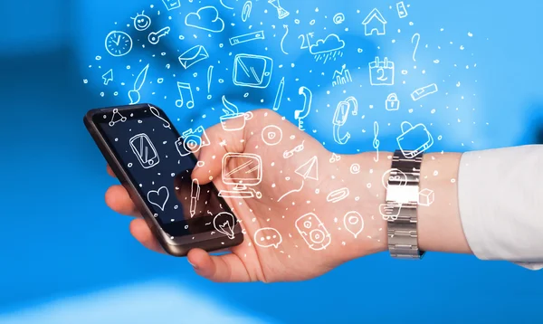 Mão segurando smartphone com ícones de mídia desenhados à mão e símbolos — Fotografia de Stock
