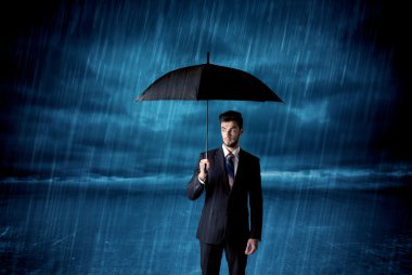 İş adamı elinde şemsiyeyle yağmurda duruyor.