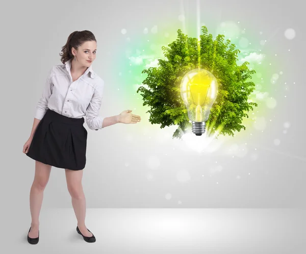 Young girl presenting idea light bulb with green tree — Stock Photo, Image