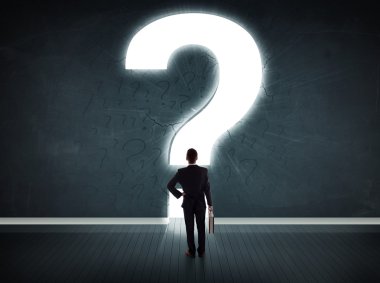 Parlak bir soru işaretiyle duvara bakan bir iş adamı 