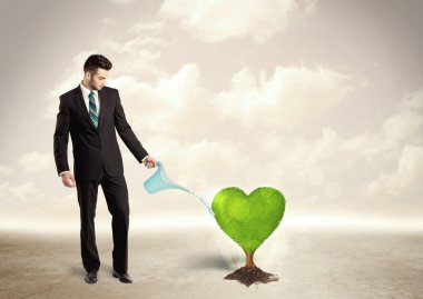 İş adamı kalp şeklindeki yeşil ağacı suluyor.