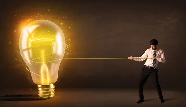 Business man pulling a big bright glowing light bulb — Stock Photo, Image