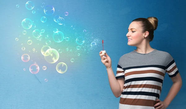 Pretty lady blowing colorful bubbles on blue background — Stock Photo, Image