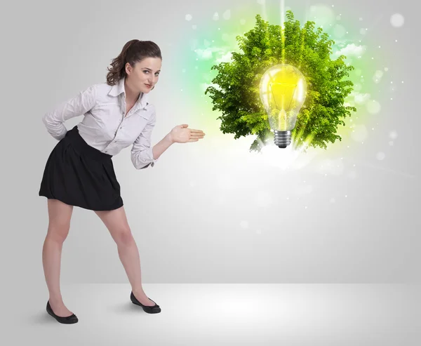 Young girl presenting idea light bulb with green tree — Stock Photo, Image