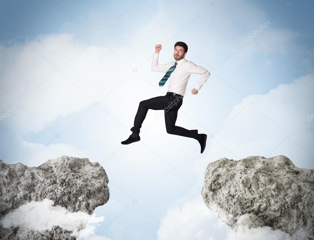 Happy business man jumping over a cliff 