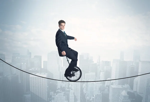 Brave guy riding a monocycle on a rope above cityscape — Stock Photo, Image