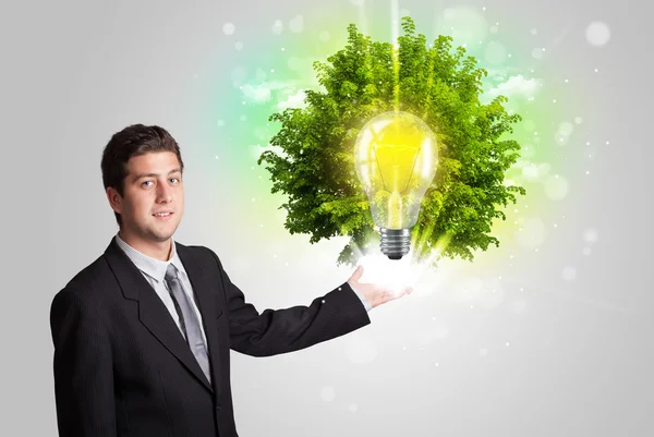 Young man presenting idea light bulb with green tree — Stock Photo, Image