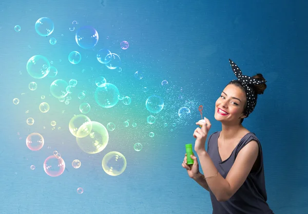 Bonita dama soplando burbujas de colores sobre fondo azul — Foto de Stock