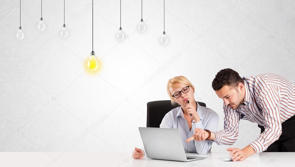 Business man and woman sitting at table with idea light bulbs