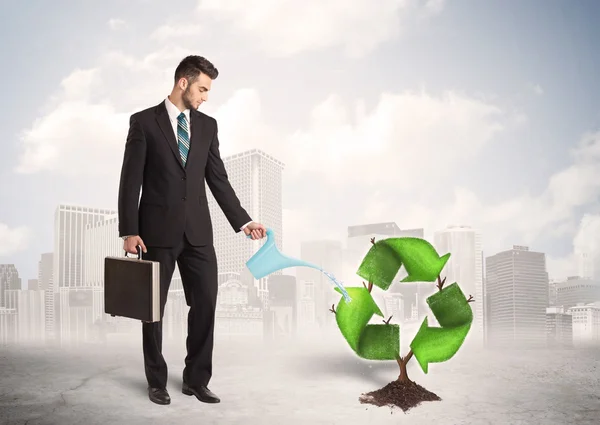 Liikemies kastelu vihreä kierrättää merkki puu kaupungin taustalla — kuvapankkivalokuva