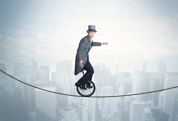 Brave guy riding a monocycle on a rope above cityscape — Stock Photo, Image