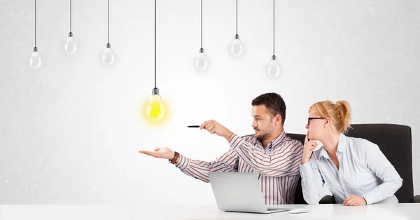 Hombre y mujer de negocios sentados a la mesa con bombillas de idea — Foto de Stock