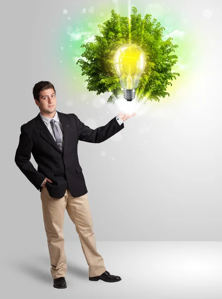 Młody człowiek prezentuje żarówkę pomysł z zielonym drzewem — Zdjęcie stockowe