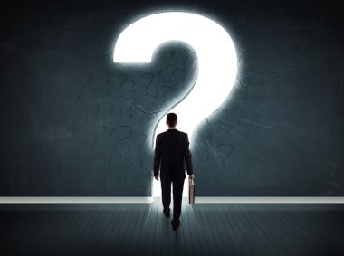 Parlak bir soru işaretiyle duvara bakan bir iş adamı 