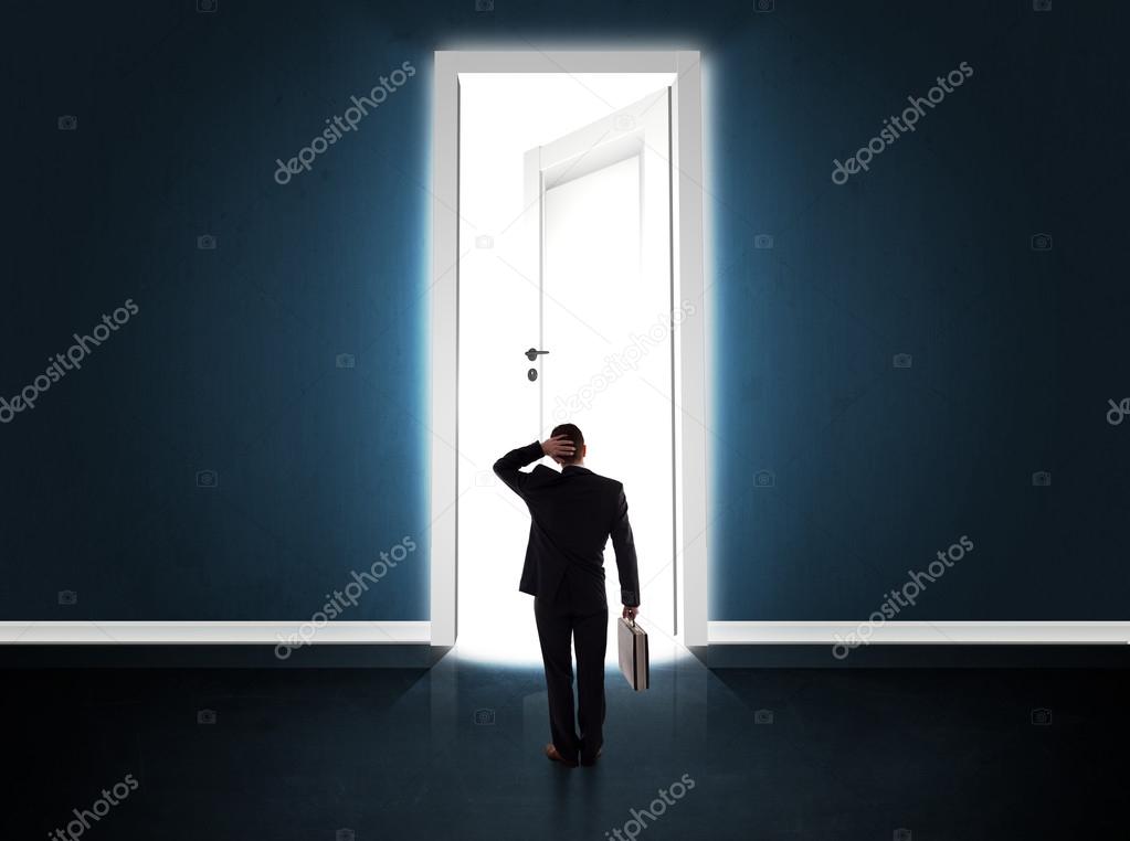 Business man looking at big bright opened door
