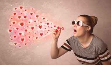 Güzel genç kız kırmızı kalp sembolleri üflüyor. 