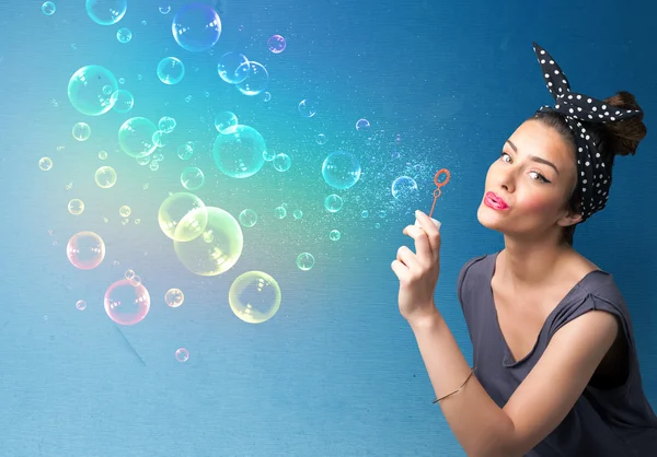 Bonita dama soplando burbujas de colores sobre fondo azul —  Fotos de Stock