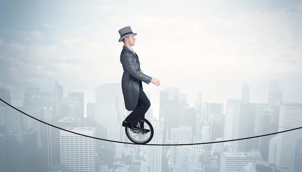 Brave guy riding a monocycle on a rope above cityscape — Stock Photo, Image